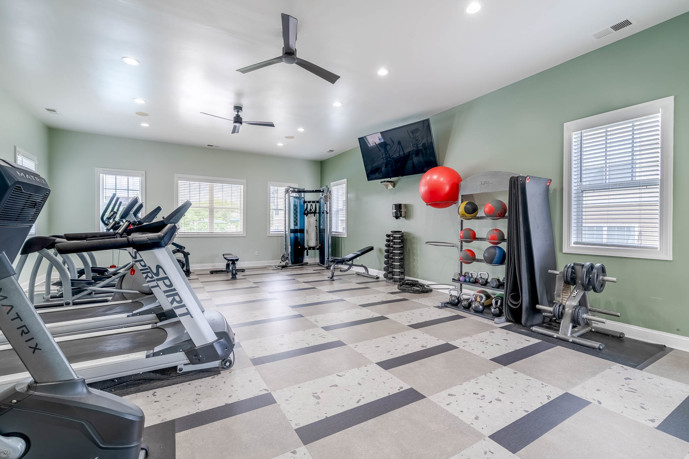 Light blue apartment community fitness center with exercise equipment, balls, and a flat screen tv